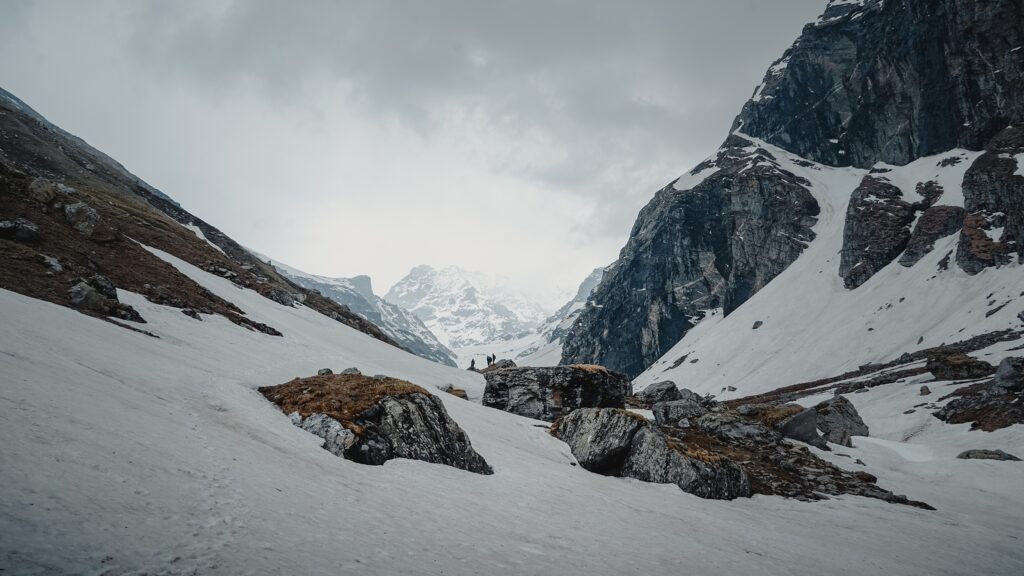 Snow-covered mountain valley with rocky slopes and distant peaks under a cloudy sky, reminiscent of the breathtaking landscapes featured in the Top 10 Treks in India for Sustainable Travel.